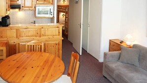 A compact living space with a wooden dining table, chairs, a sofa, a kitchenette with a microwave, and a bed in the background.