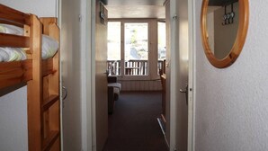 A narrow hallway leading to a balcony with a wooden bench and a view of a parking area.
