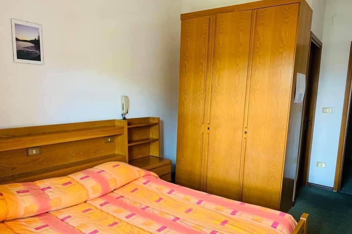 A bedroom with a bed, wooden wardrobe, and a nightstand.