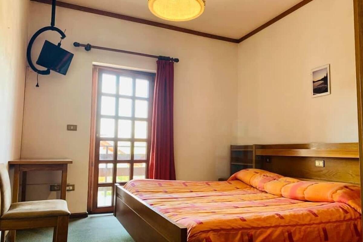 A bedroom with a bed, a chair, a desk, a window with curtains, and a ceiling light fixture.