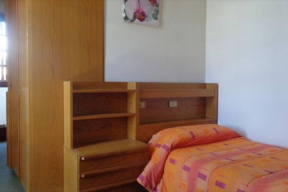 A bedroom with a wooden bed frame, a built-in shelf unit, and a colorful bedspread.