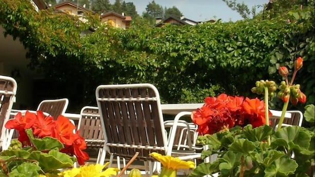 An outdoor seating area with metal chairs and tables, surrounded by flowering plants. - La Scardola Ristorante Hotel Bar (Baselga di Pine)