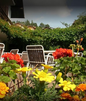 An outdoor seating area with metal chairs and tables, surrounded by flowering plants. - La Scardola Ristorante Hotel Bar (Baselga di Pine)
