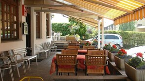 An outdoor cafe with wooden tables and chairs, a covered seating area, and potted plants. - La Scardola Ristorante Hotel Bar (Baselga di Pine)