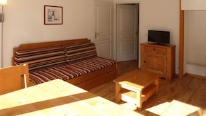 A small, cozy room with a striped sofa, a wooden table, a television on a wooden cabinet, and a framed picture on the wall. - Spacious 3-Room Apartment for 8 with Heated Pool & Terrace in Les Orres 1800 (Les Orres)