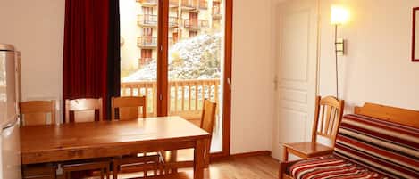 Ein gemütlicher Raum mit einem Holzesstisch, Stühlen, einer Bank, einer Couch mit gestreifter Kissen und einer Schiebetür zu einem Balkon, sowie einer Wandlampe.
