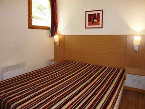 Ein Einzelbett mit gestreifter Bettdecke, ein hölzernes Kopfteil, zwei Nachttischlampen, ein Fenster mit Vorhang und ein gerahmtes Bild an der Wand.