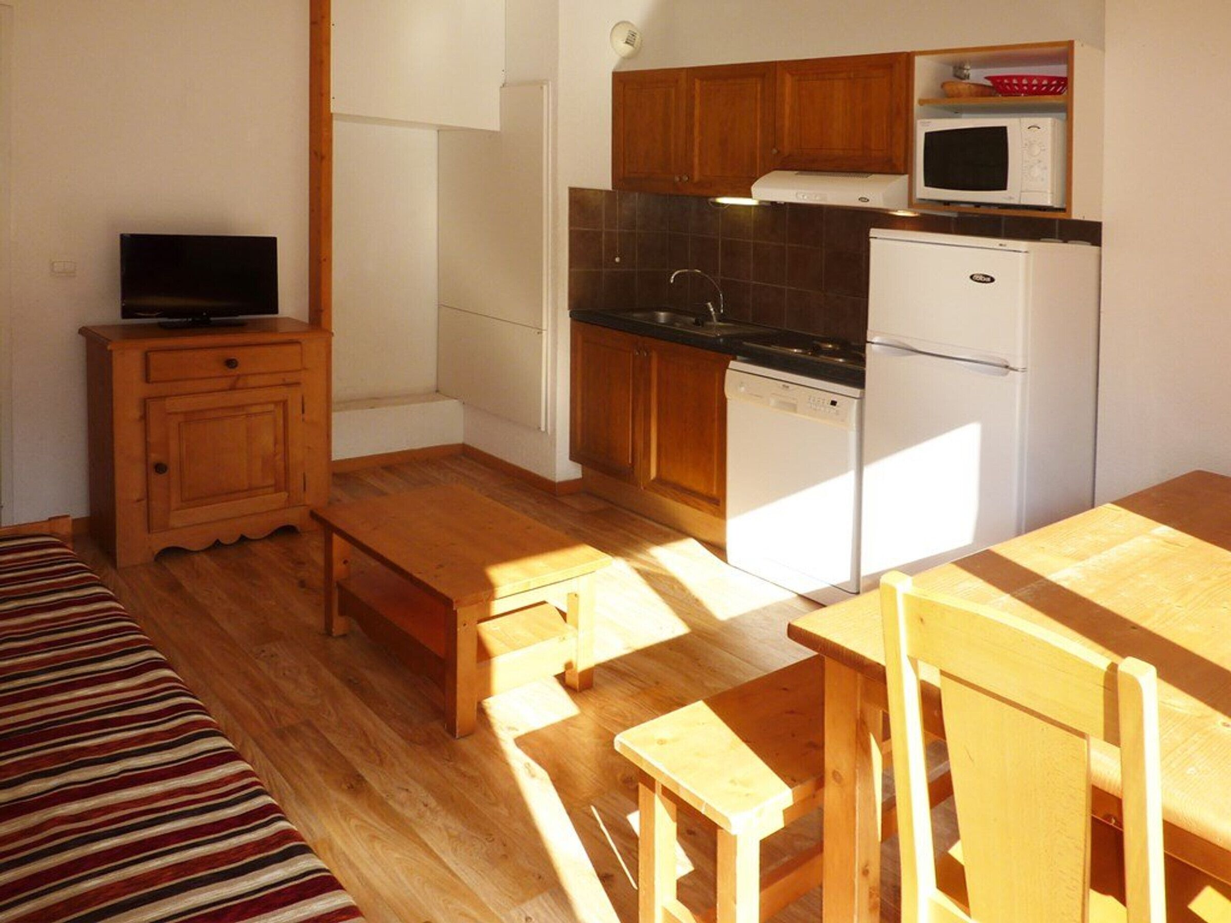 Una cocina compacta con armarios de madera, microondas, lavavajillas y comedor con banco y mesa.
