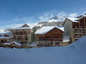 A cluster of wooden cabins with balconies, set against a snowy mountain backdrop. - Spacious 3-Room Apartment for 8 with Heated Pool & Terrace in Les Orres 1800 (Les Orres)