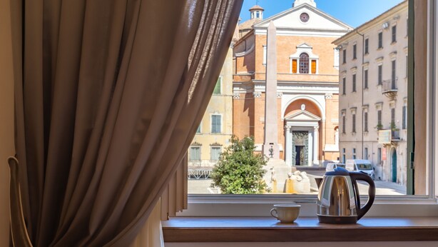 A window with a view of a building with a large archway and a bell tower. - Dimora Storica Lo Svevo (Jesi)