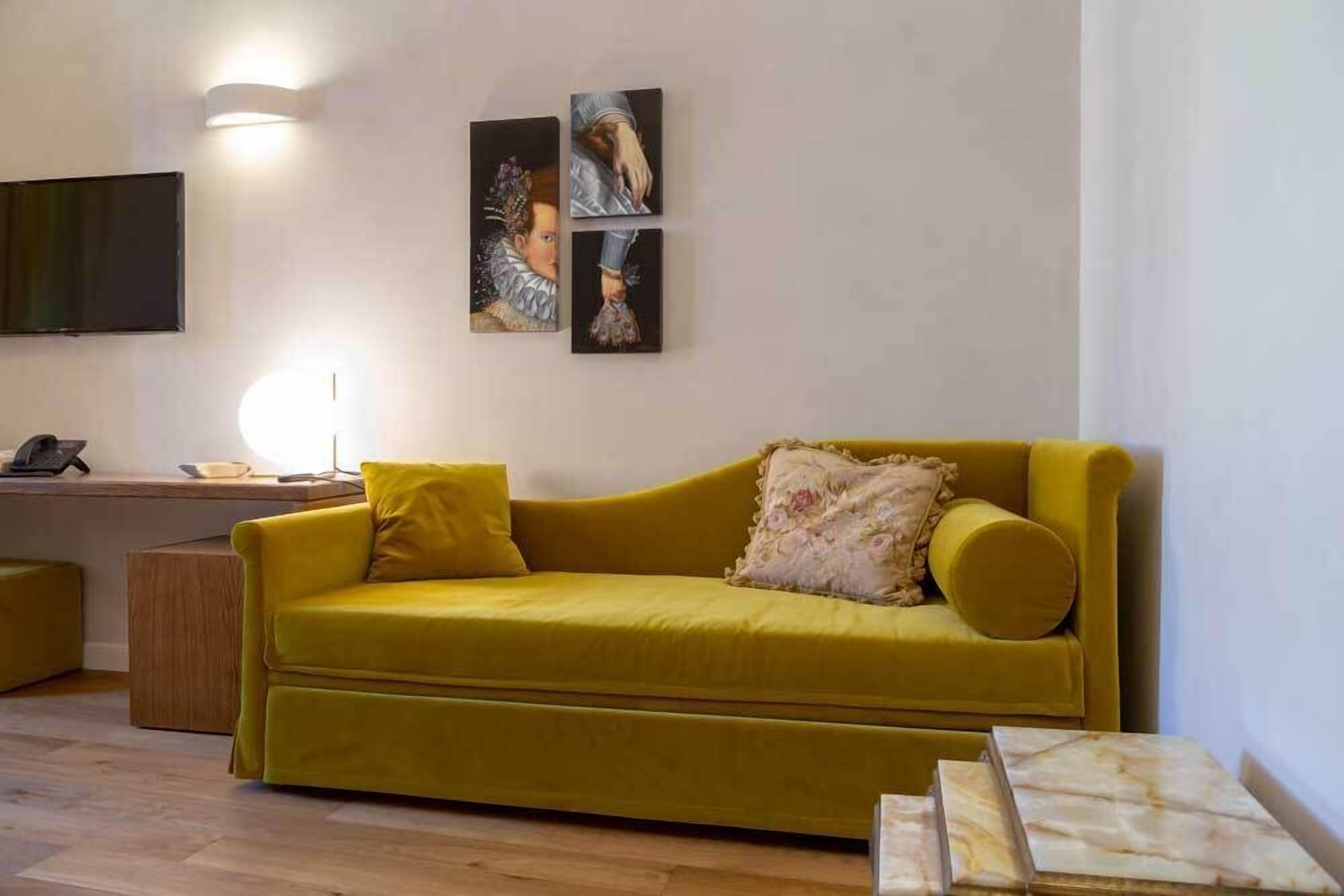 Ein gelbes Sofa mit floralen Kissen, ein an der Wand befestigter Flachbildfernseher und ein kleiner Holztisch mit einer Lampe.