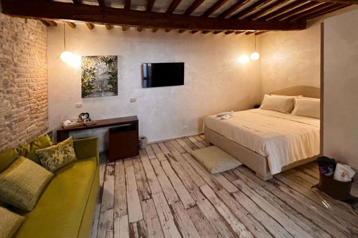 Une pièce avec un lit, un canapé vert, un téléviseur fixé au mur et un plancher en bois.