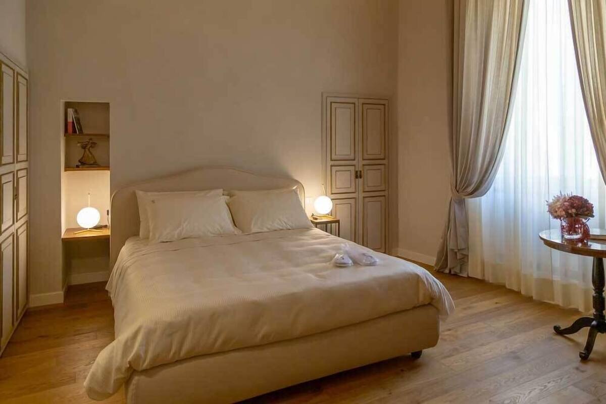Un dormitorio ordenado con una cama grande, lámparas de noche, una mesita con un florero y un armario.