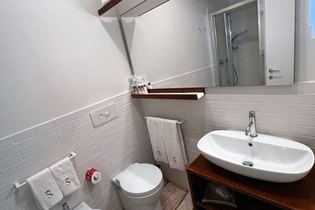 A bathroom with a white sink, a toilet, a towel rack, and a shower area.
