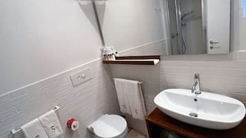A bathroom with a white sink, a toilet, a towel rack, and a shower area.