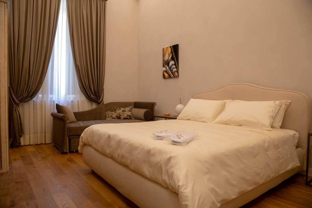 Un dormitorio con una cama grande, un sofá, una mesita de noche y un cuadro en la pared.
