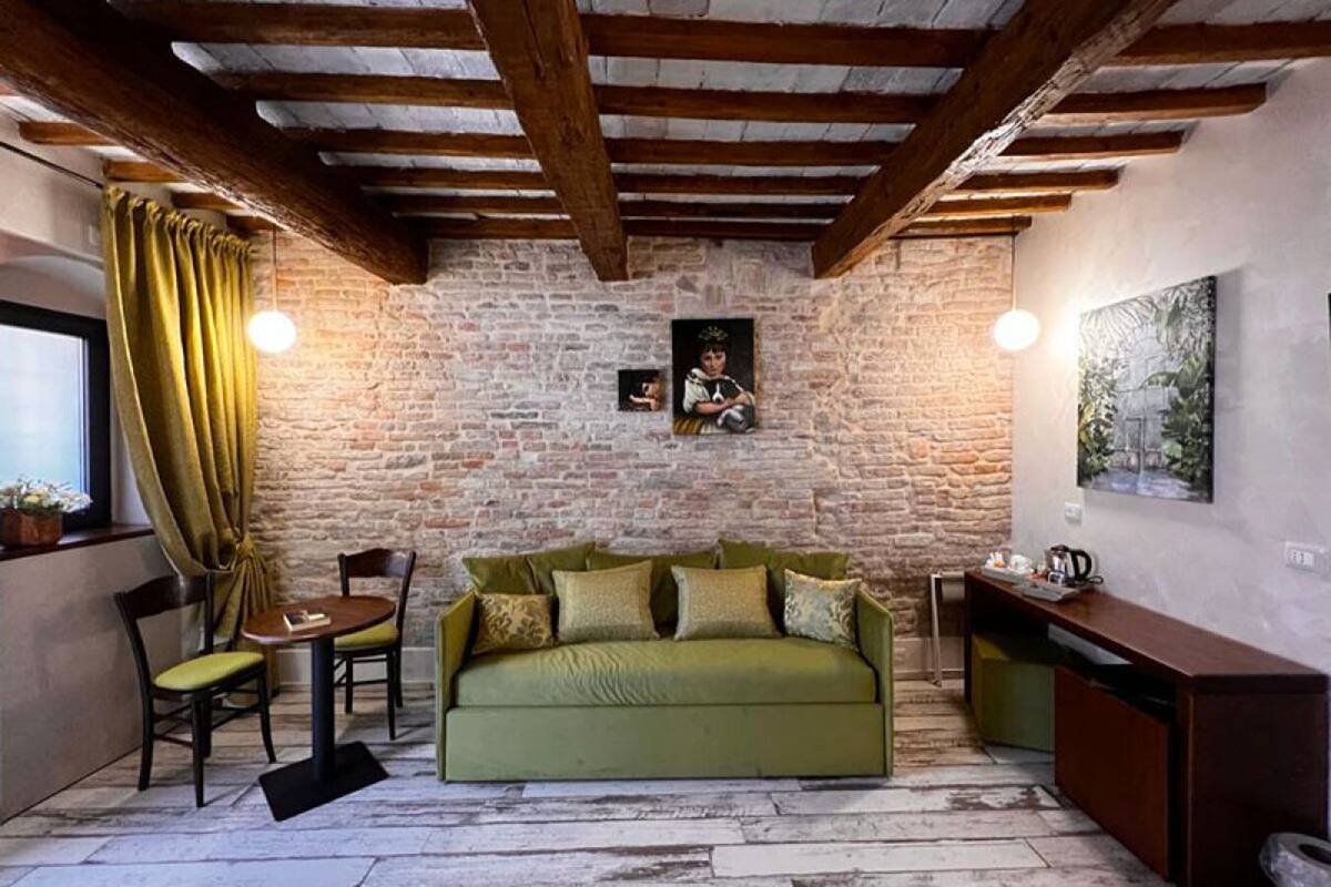 Una habitación acogedora con un sofá verde, una mesita y sillas. Se observa una pared de ladrillo con un marco de foto y un cuadro.