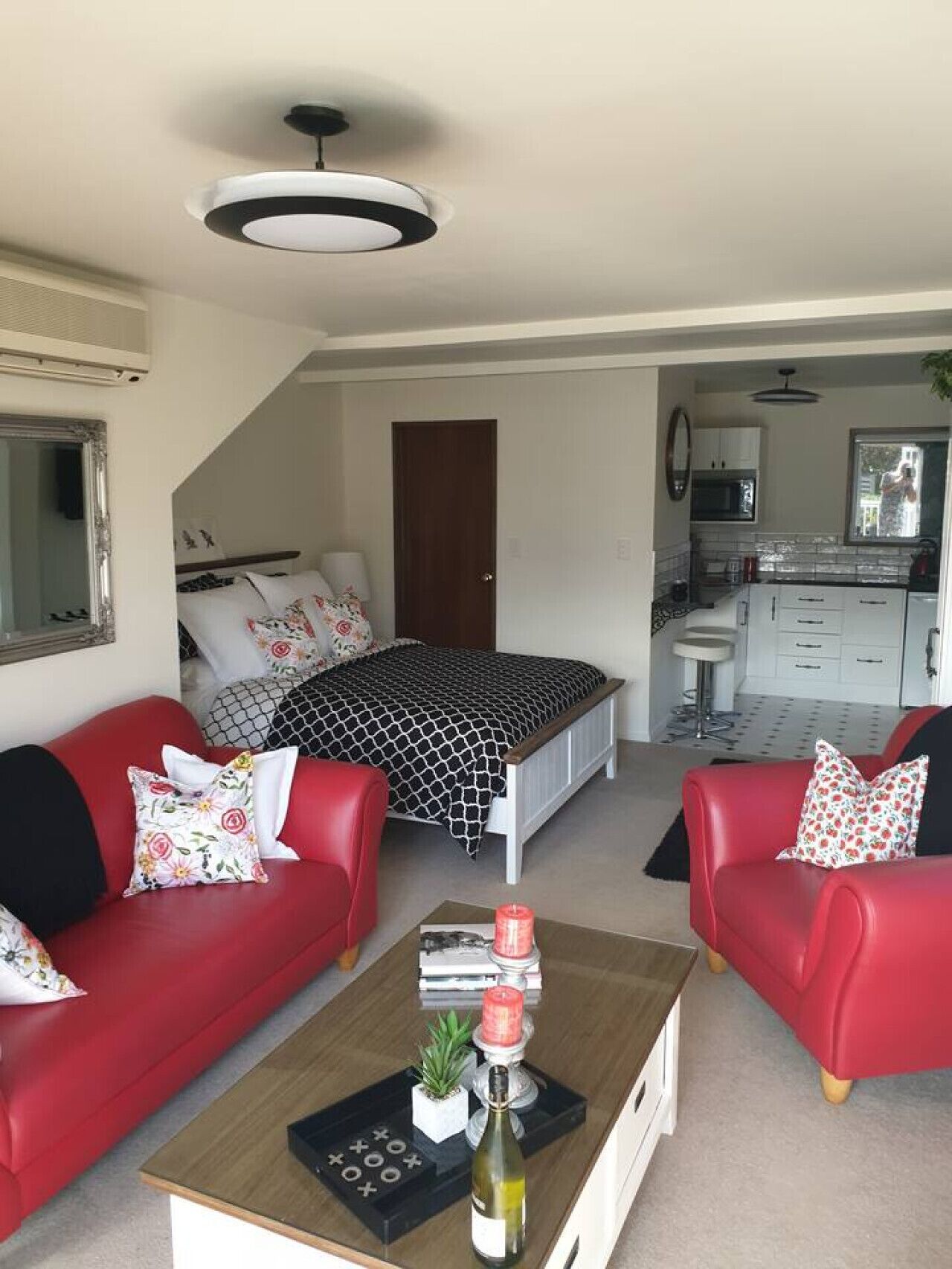 A modern, compact living space with a bed, two red sofas, a coffee table, and a kitchenette.