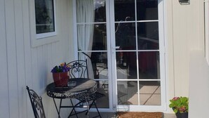 A covered patio with a table and chairs, a small potted plant, and a sliding glass door leading to an outdoor area. - Tui2 - Studio (Macandrew Bay)