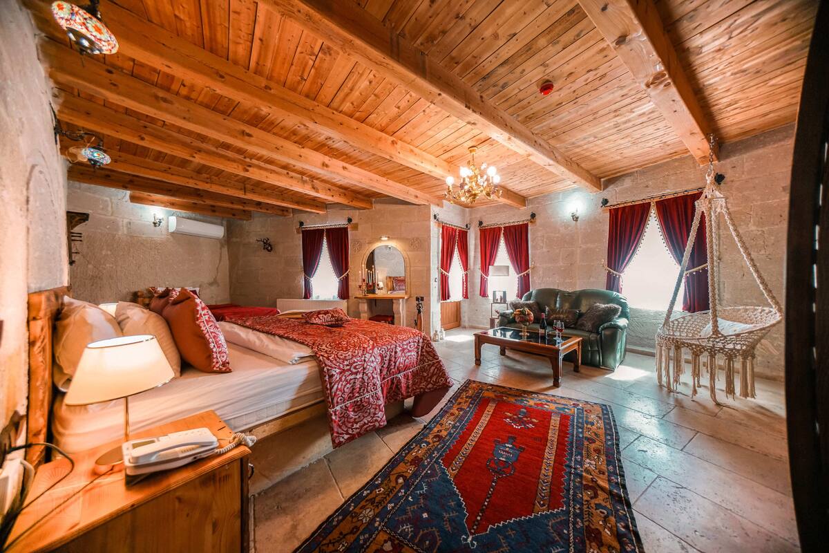 A cozy room with wooden beams, a bed with red bedding, a sofa, a coffee table, and a hanging chair.