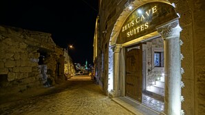 A stone building with a sign reading "ZEUS CAVE SUITES" at night.