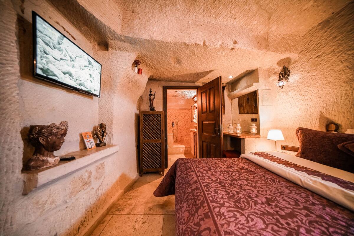 A cozy room with a bed, a television mounted on the wall, and a shelf with decorative items.