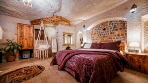 A rustic bedroom with a stone wall, wooden furniture, and a hanging chair.