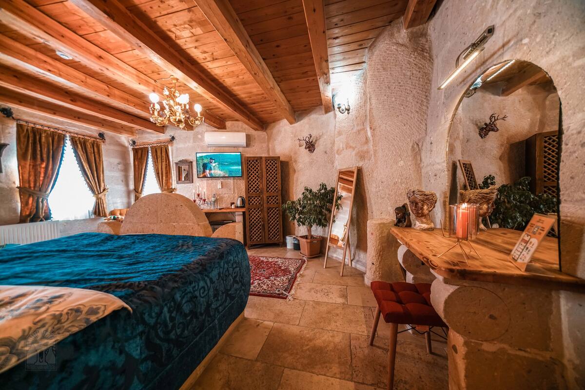 A cozy bedroom with a wooden ceiling, a bed with a blue bedspread, a desk with a computer, a television, and a mirror.