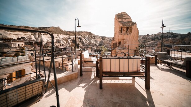 A rooftop terrace with a stone bench, a metal railing, and a view of a mountainous landscape.