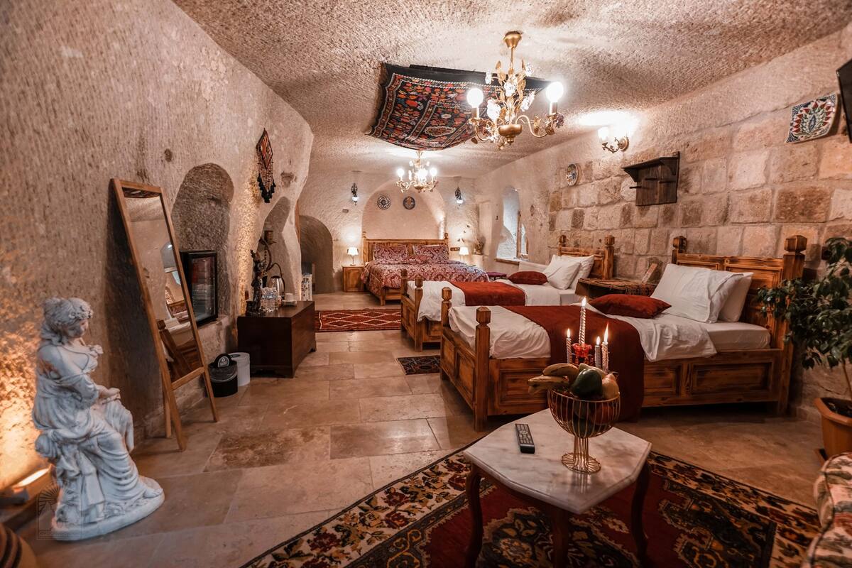 A traditional room with stone walls, a wooden bed, a small table with a candle, and a statue.