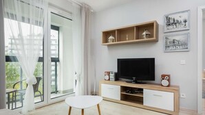 A modern living room with a TV, wooden shelves, and artwork on the wall. - Elegant Apartment | Balcony | Workspace (Warszawa)