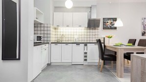A modern kitchen with white cabinets, a microwave, and a dining area with a table and chairs. - Elegant Apartment | Balcony | Workspace (Warszawa)