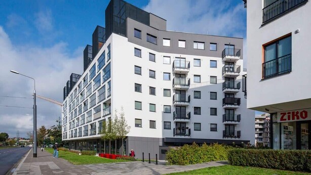 A modern multi-story building with a white facade, multiple balconies, and a visible storefront with signage. - Elegant Apartment | Balcony | Workspace (Warszawa)