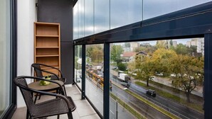 A balcony with wicker chairs and a small wooden shelf, overlooking a city street with vehicles and trees. - Elegant Apartment | Balcony | Workspace (Warszawa)