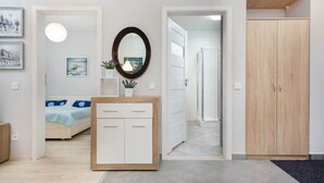 A modern bedroom with a bed, bedside table, and a mirror. There is a hallway leading to a bathroom and a wardrobe. - Elegant Apartment | Balcony | Workspace (Warszawa)