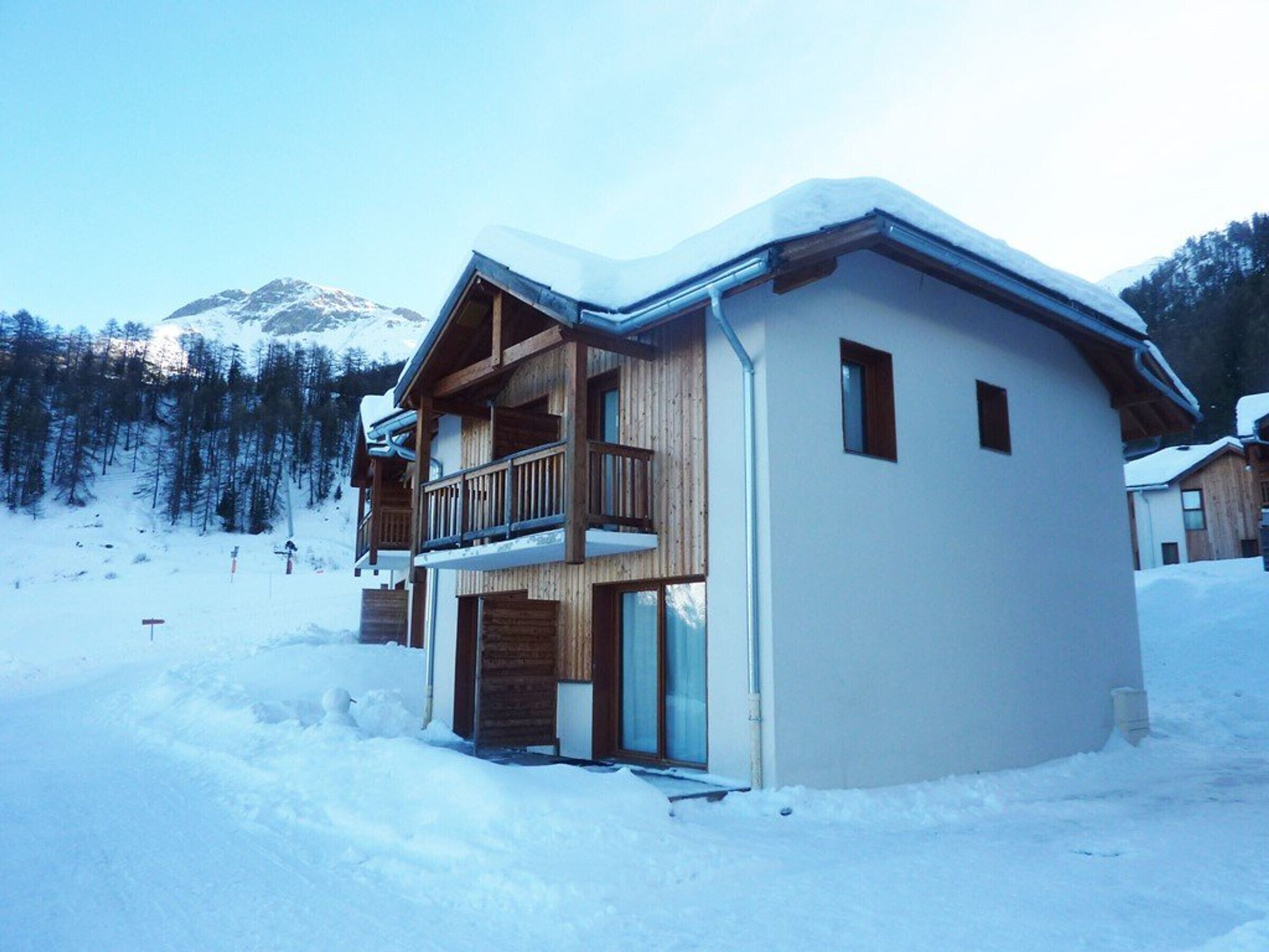 Eine zweistöckige Holzhütte mit Balkon, eingebettet in eine verschneite Berglandschaft.