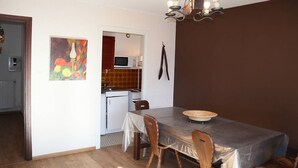 Uma área de refeições com mesa e cadeiras, cozinha ao fundo e um quadro na parede.