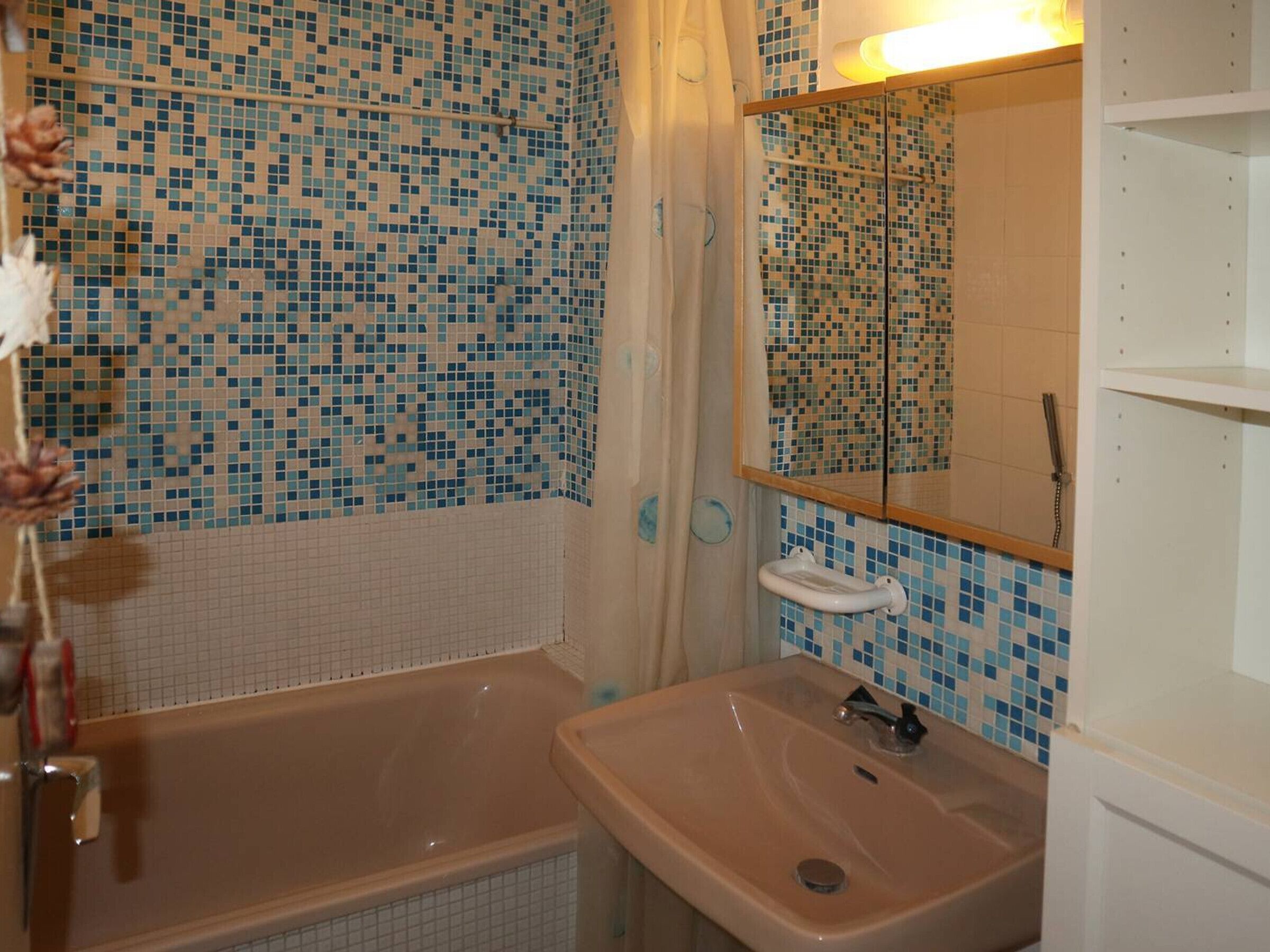 Ein Badezimmer mit einer Wand aus Mosaikfliesen, einer Badewanne, einem Waschbecken mit Spiegel und einem Handtuchhalter.