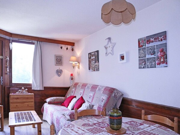 A cozy bedroom with a wooden bed, a small table, and a window with curtains.