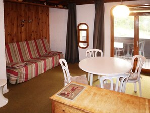 A cozy room with a striped sofa, a round table with chairs, and a wooden cabinet. - Cozy Studio Central Location, Ski-In/Ski-Out, Sleeps 4, South-Facing Balcony (Les Orres)