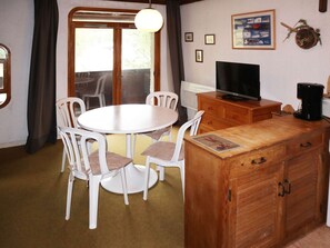 A dining area with a round table and white chairs, a wooden cabinet with a television, and a coffee maker. - Cozy Studio Central Location, Ski-In/Ski-Out, Sleeps 4, South-Facing Balcony (Les Orres)