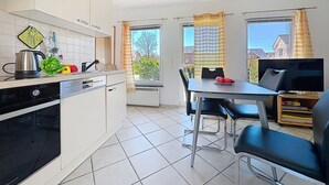 Cocina compacta con lavavajillas, tetera y comedor con mesa y sillas.