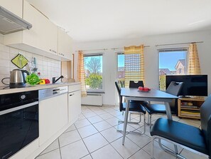 Een kleine keuken met een vaatwasser, waterkoker en een eethoek met een tafel en stoelen.