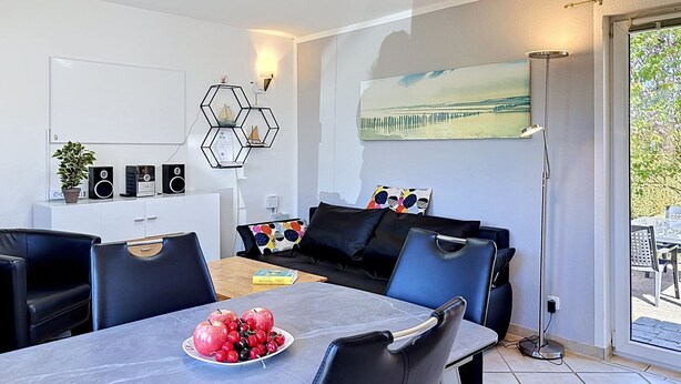 Una sala de estar moderna con comedor, un sofá, una mesa de centro con fruta y un cuadro en la pared.