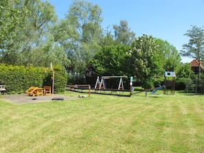 Explore a serene outdoor play area surrounded by lush greenery and trees, featuring a swing set, slide, and climbing structure.