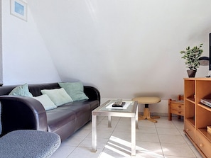 A modern living room with a leather sofa, a glass coffee table, a wooden side table, and a bookshelf.