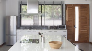 A modern kitchen with a central island, stainless steel appliances, and a view of the outdoors through large windows. - Bliss Villas (Ko Pha-ngan)