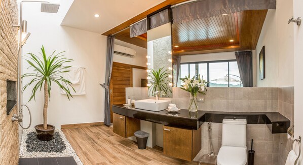 Un baño moderno con tocador de madera, un espejo grande y un inodoro. Hay dos plantas en macetas y un lavamanos con un espejo encima.