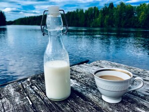 Una botella de vidrio con leche y una taza blanca sobre una superficie de madera junto a un lago.