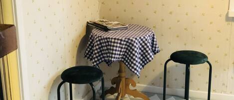 A corner room with a checkered tablecloth, two stools, and patterned wallpaper.